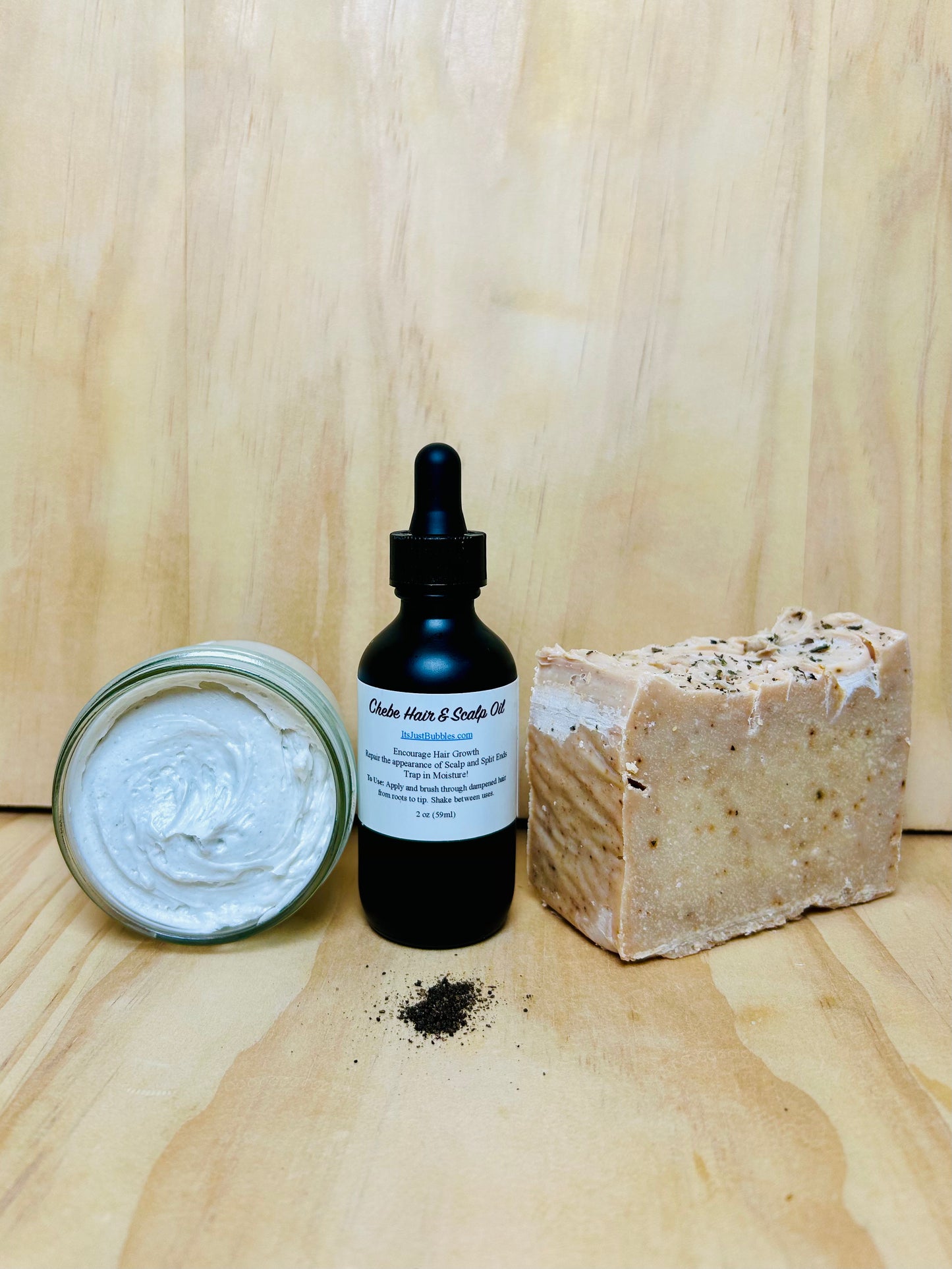 A set of hair care products including a jar of whipped butter, a dropper bottle of oil, and a bar of solid shampoo or conditioner, all placed on a wooden surface.