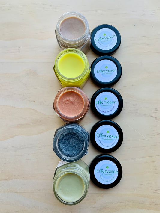 A set of glass jars with various colored cream face masks on a wooden surface.